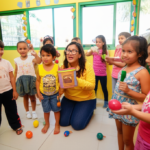 Crianças pequenas felizes participando de uma aula de histórias e brincadeiras cantadas com uma professora sorridente, usando instrumentos musicais infantis e recursos visuais lúdicos em sala de aula.